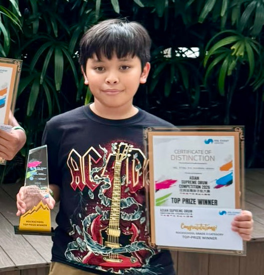 Haz Ryean holding Certificate of Distinction Top Prize Winner trophy for Rockschool Grade 3 at Asian Supreme Drum Competition ASDC 2026 Singapore wearing AC/DC t-shirt